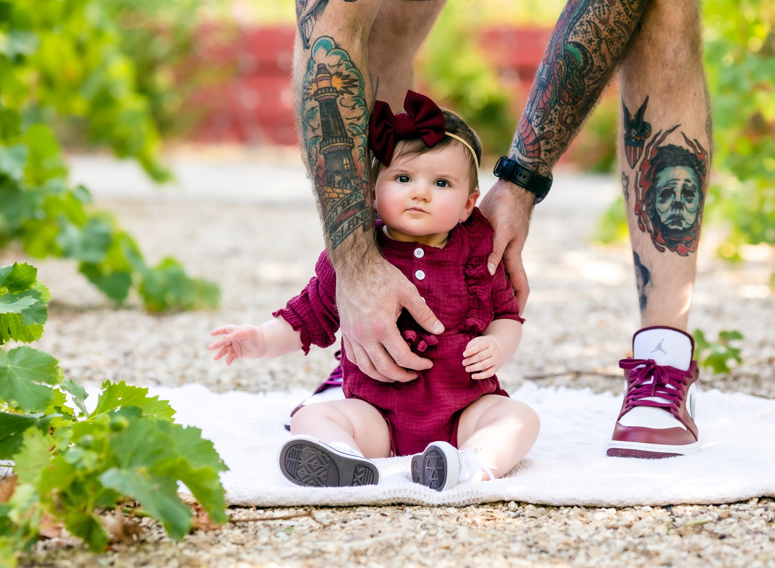 picture of infant girl wearing burgundy red with dad's tattooed arms in the photo